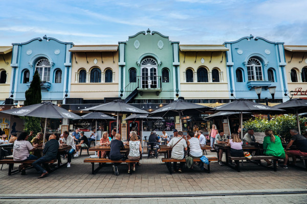 Colourful facades of the art deco buildings along New Regent Street in central Christchurch. A summer day with people sharing kai outdoors under shade umbrellas