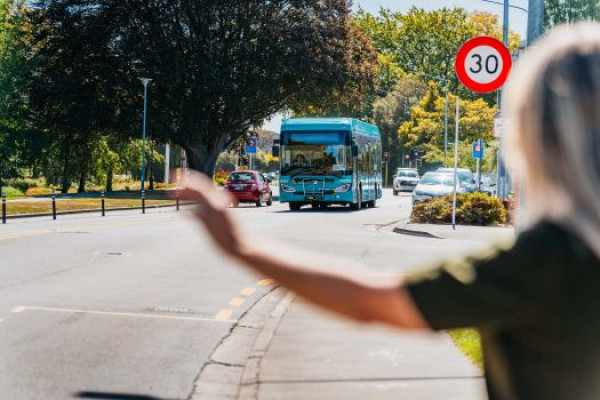 A woman raises her arm to signal as a teal Metro bus approaches in the background